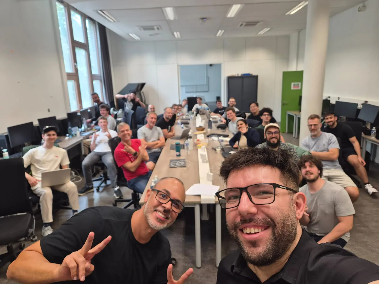 A group selfie in a workshop room: Anderson, front left, makes a peace sign, with about twenty developers at long desks behind him