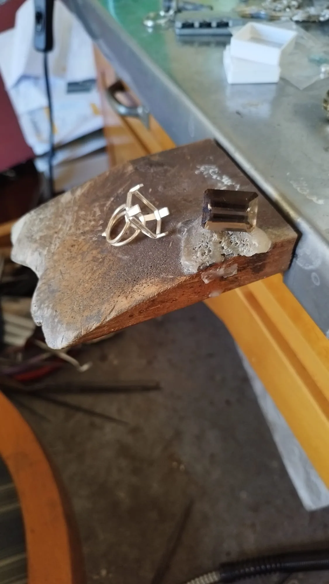 A hand-built silver basket setting on the bench, an emerald-cut smoky quartz beside it