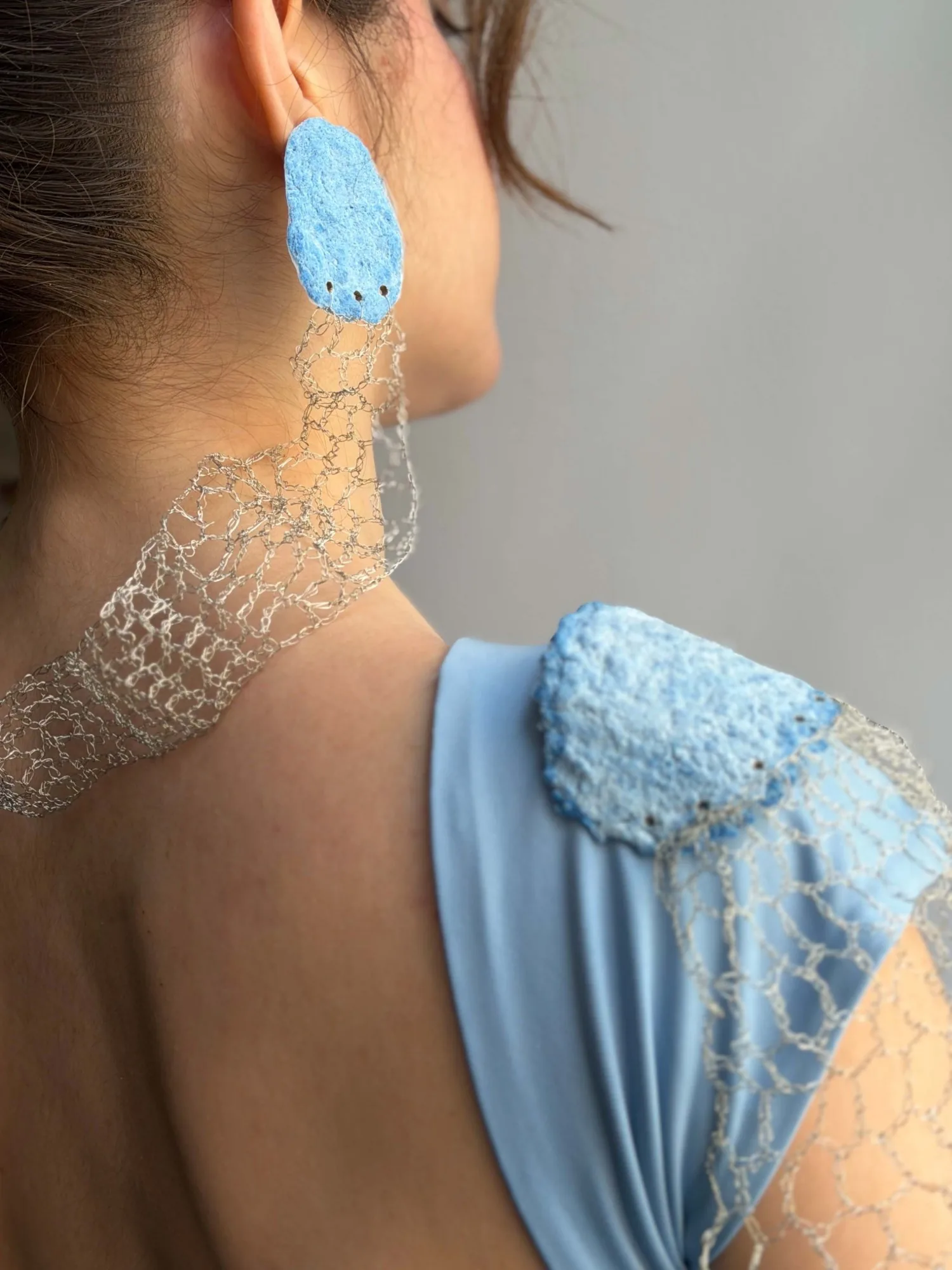 Seen from behind: the earring at the ear and the wire mesh collar around the neck, with the shoulder piece on the sleeve