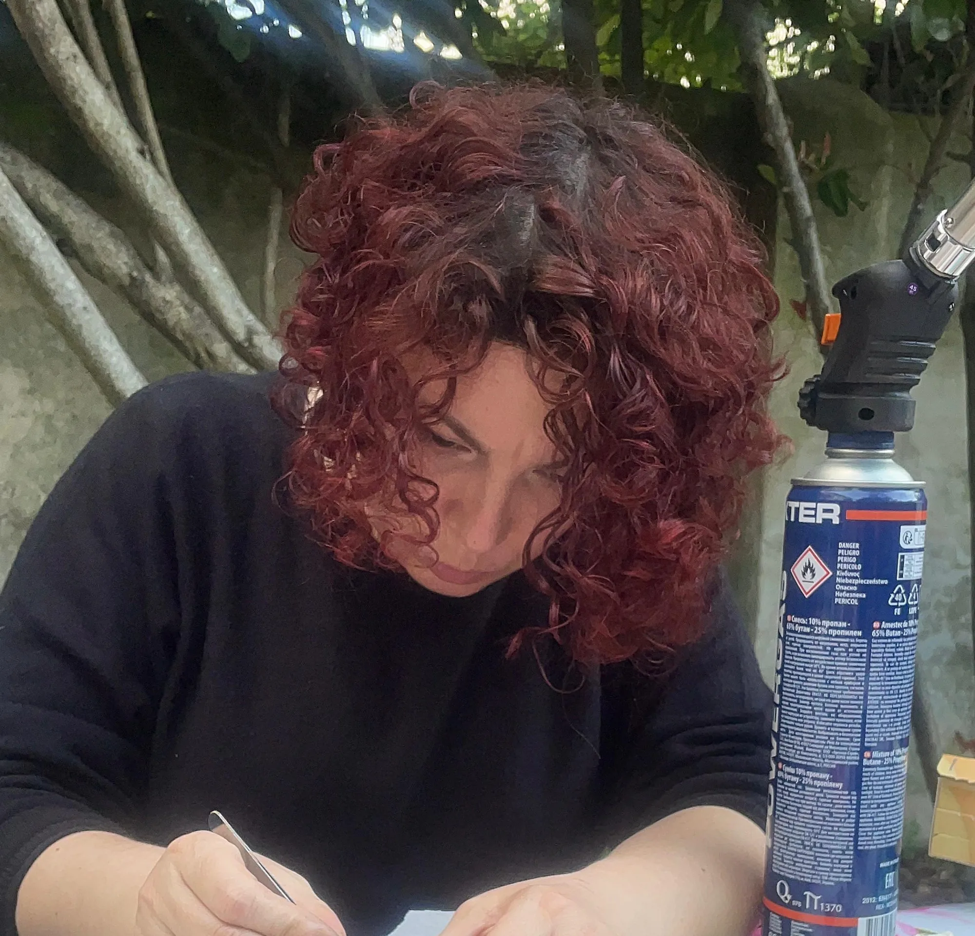 Cadia at a bench outdoors, soldering with a hand torch