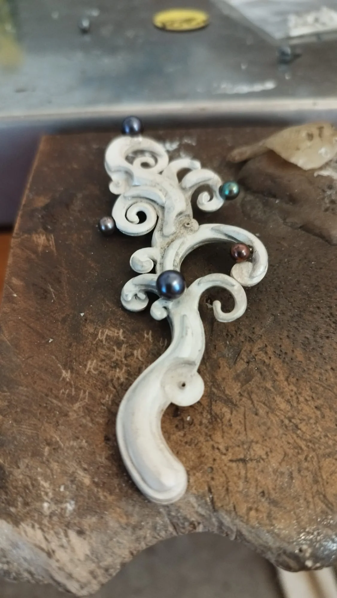 The same scrolled pendant, finished, lying on the bench