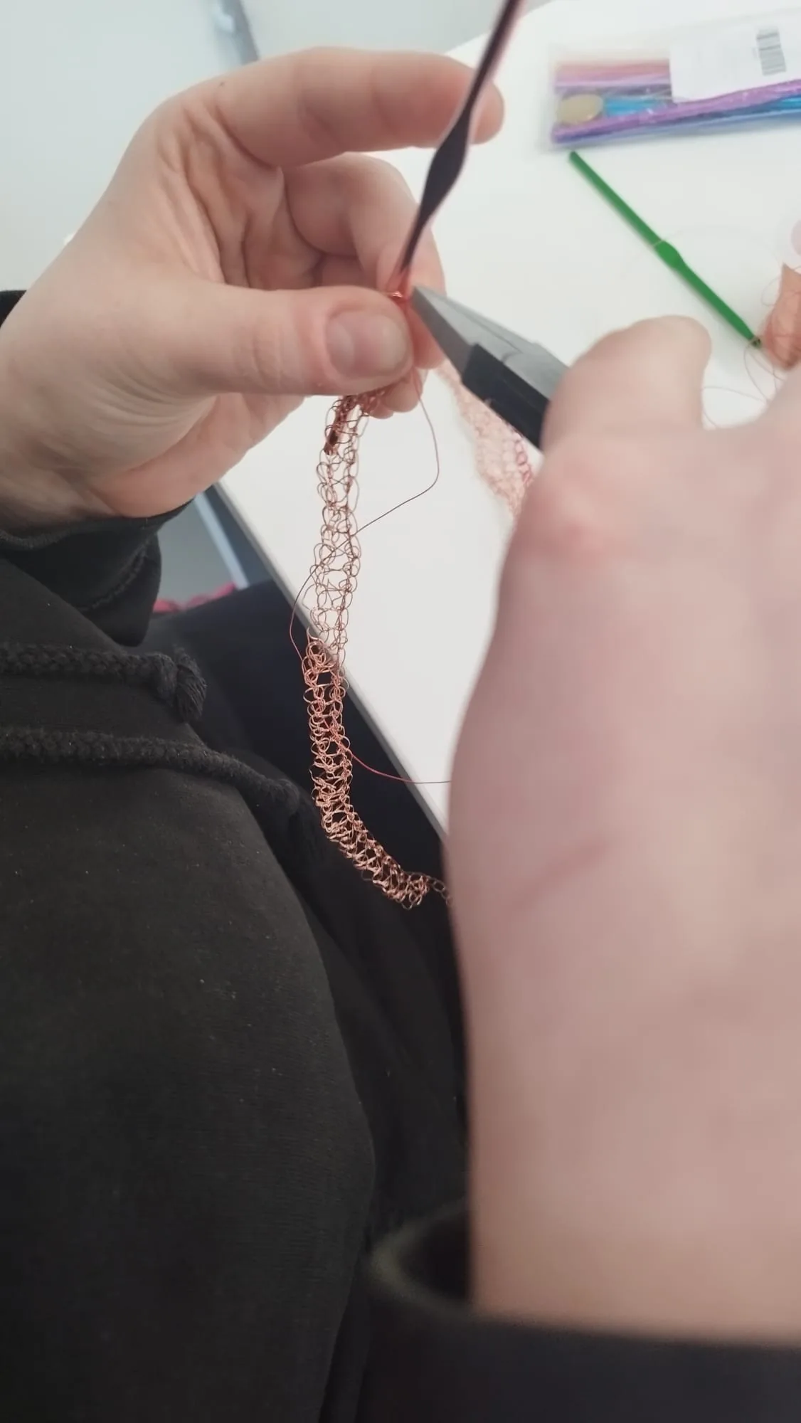 Hands crocheting copper wire with a crochet hook