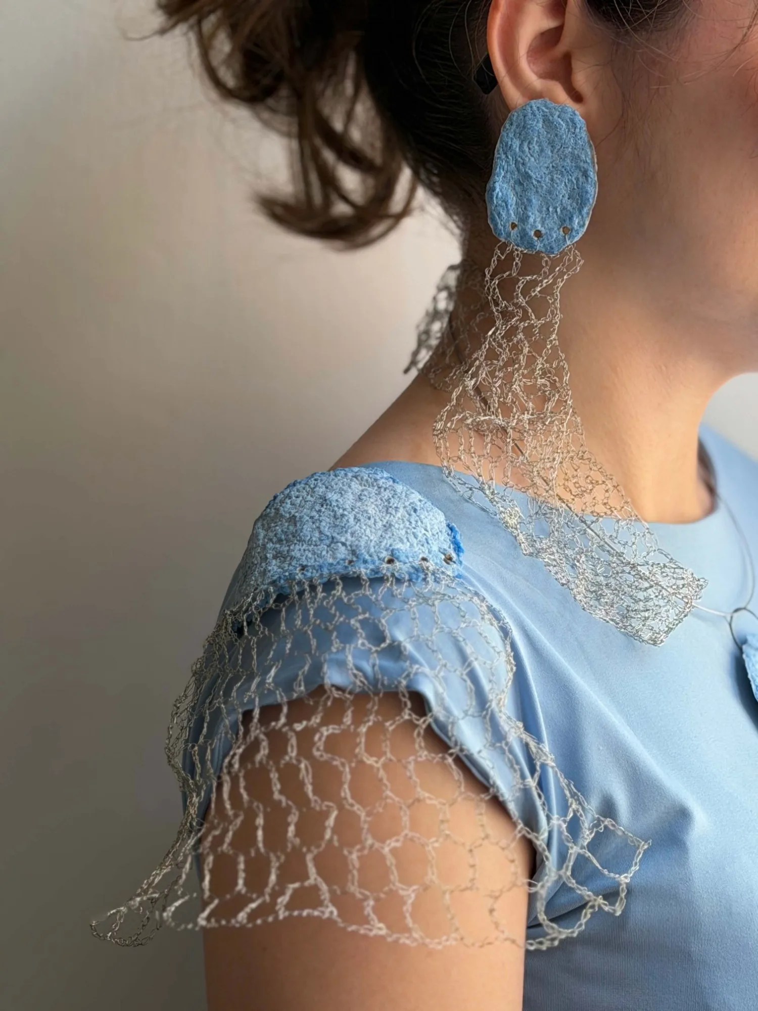 A set worn with a blue top: a blue textured earring with a wire mesh drop, a wire mesh collar, and a matching shoulder piece over the sleeve