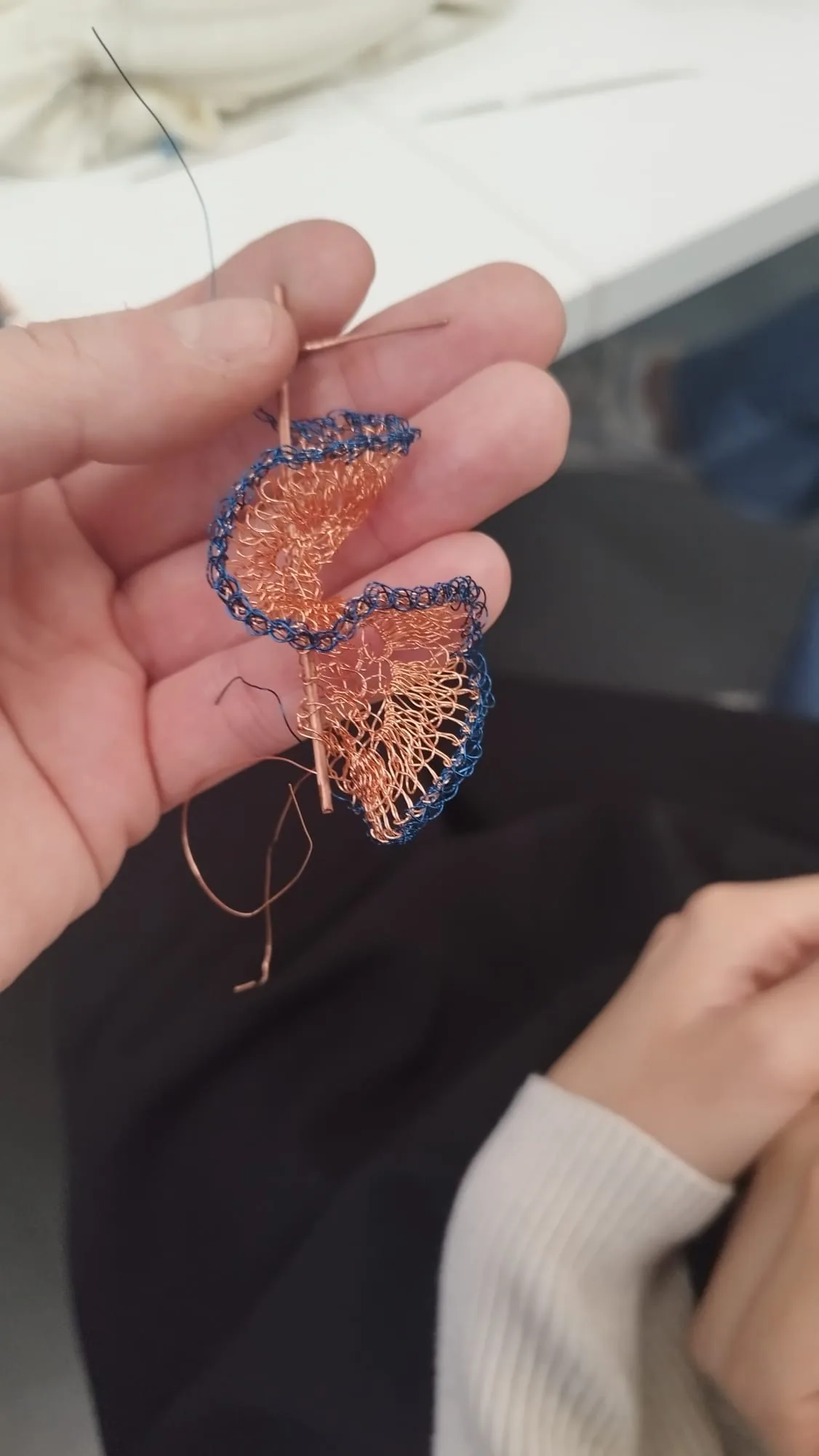 A crocheted copper wire spiral with a blue edge, held in two hands